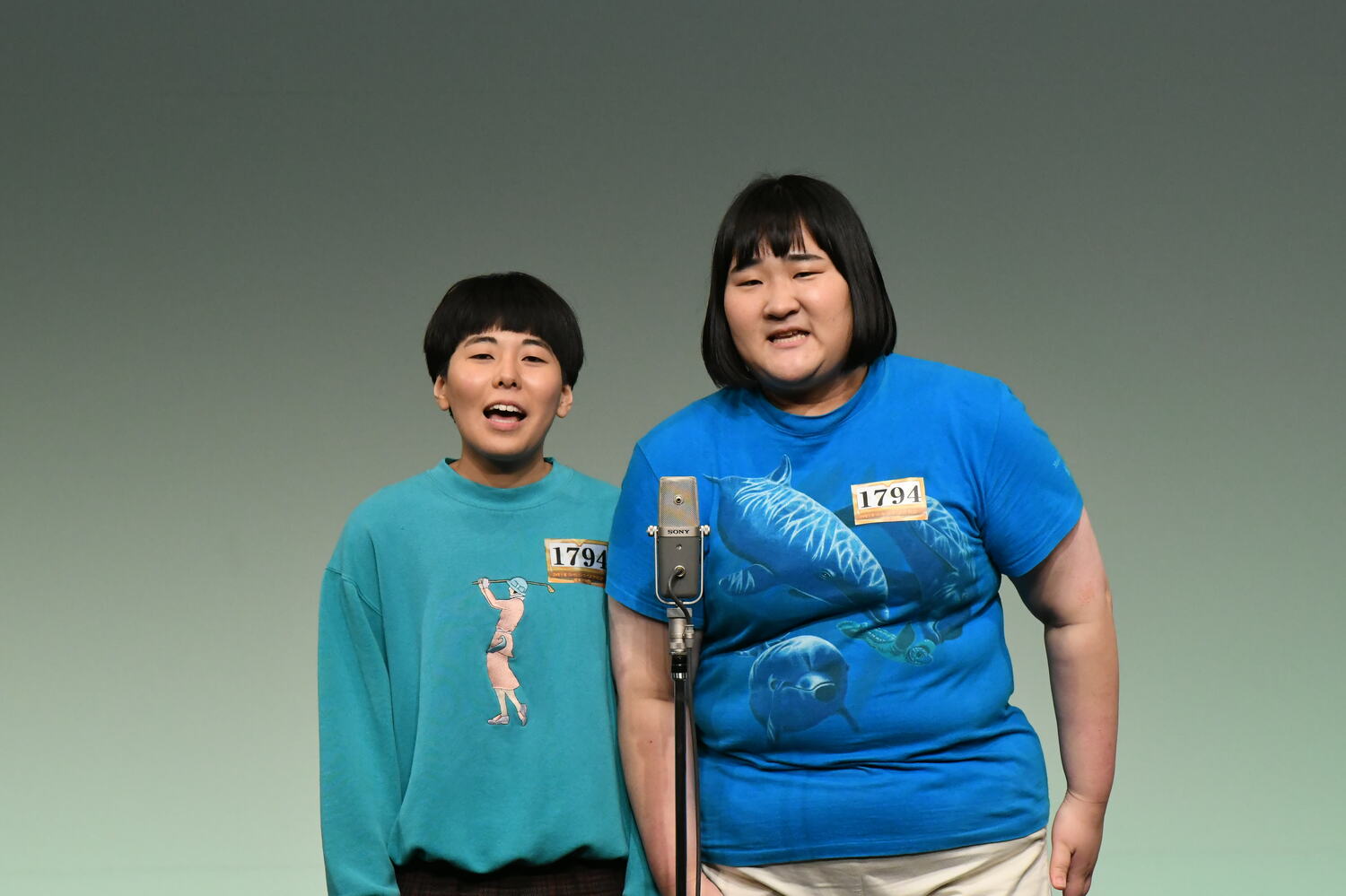 愛は青のイルカのTシャツ、誠は貴婦人がゴルフしている緑のTシャツ ©M-1グランプリ事務局