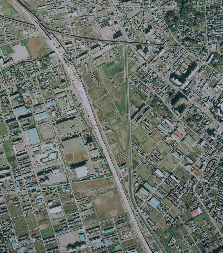 1984年に撮影された武蔵浦和付近の航空写真。中央左、大きな四角が3つ並ぶのがロッテ浦和工場。翌85年に埼京線が開業するが、写真左上～右下へ線路工事が進んでいることが分かる　出典：国土地理院の空中写真