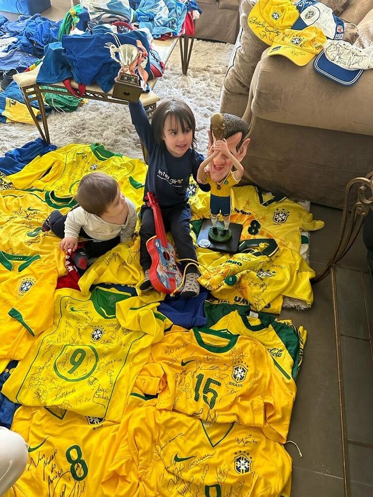 ドゥンガの二人の孫娘が、セレソンのユニフォームの山の中に。女の子が左手に持っているのは、「1994年ワールドカップで優勝カップを掲げるドゥンガ」の特製人形（全27枚中の26枚目）　※本人提供