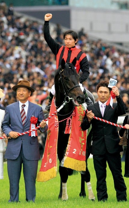 ダービーの口取り式でエイシンフラッシュの隣に立った久保は岩本厩務員の写真を掲げた　Tomohiko Hayashi