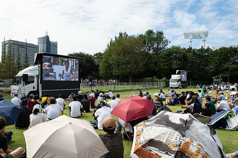 神宮外苑の芝生広場でのパブリックビューイング。先頭を走る設楽が映し出される。 ／ photograph by Nanae Suzuki
