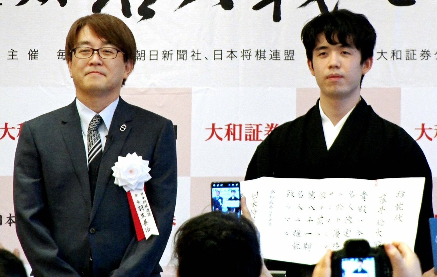 史上最年少で獲得した将棋の名人就位式で、推戴状を手にする藤井聡太七冠（右）。左は日本将棋連盟の羽生善治会長　©JIJI PRESS