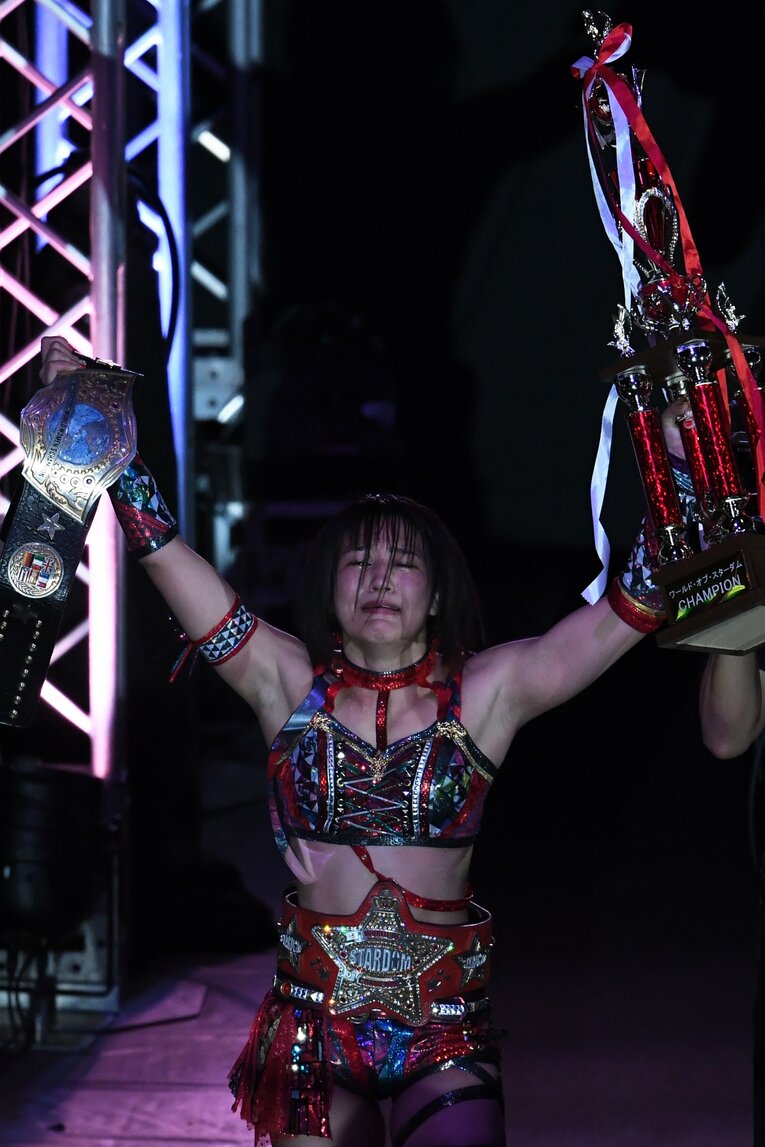 赤いベルトを腰に巻き、トロフィーを掲げる朱里