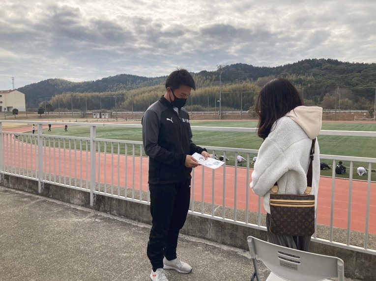 来場者に飲み物のメニューを見せるサッカー部員　©︎Takagawa Gakuen