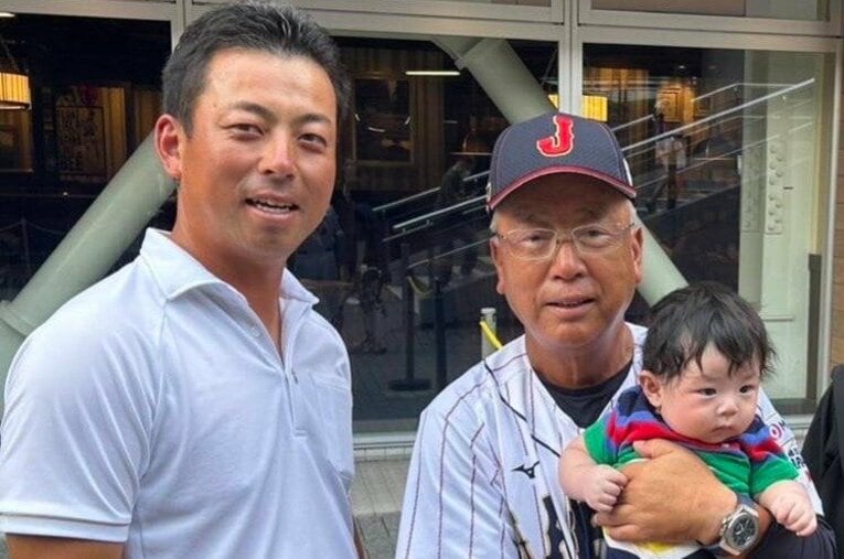 孫の遼正（りょうま）くんを抱き笑顔の明徳義塾高校・馬淵史郎監督（右）。息子で拓殖大の馬淵烈監督（左）は、侍ジャパンU-18 代表を率いた父の応援にも駆け付けた　©馬淵烈さん提供