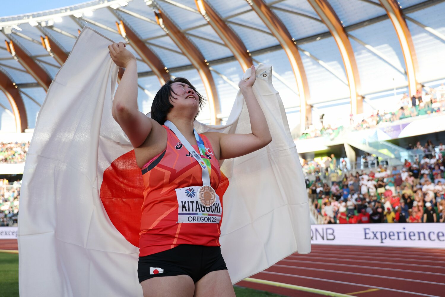 日本女子史上初の銅メダルを獲得し涙を流して日の丸を背に掲げる北口榛花 ©︎Getty Images