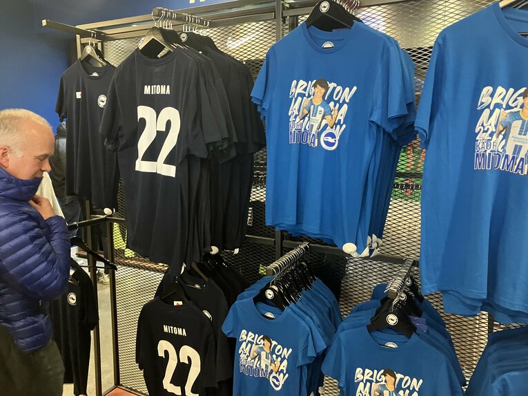 右のブルーのTシャツがオリジナルデザインの三笘Tシャツ。「おそらく店一番の人気商品になると思う」（店員のジェイミー・ハリアさん）