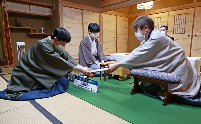 第72期王将戦７番勝負第２局、立会人の谷川浩司十七世名人（左）に封じ手を渡す羽生善治九段（右）。中央は藤井聡太王将（代表撮影）©JIJI PRESS