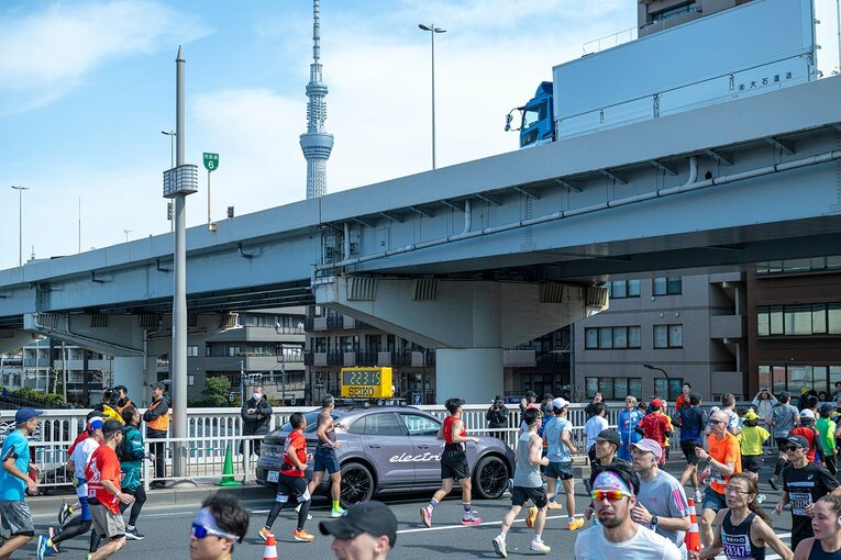 東京スカイツリーとポルシェの計時車を眺めるランナー達　©東京マラソン財団
