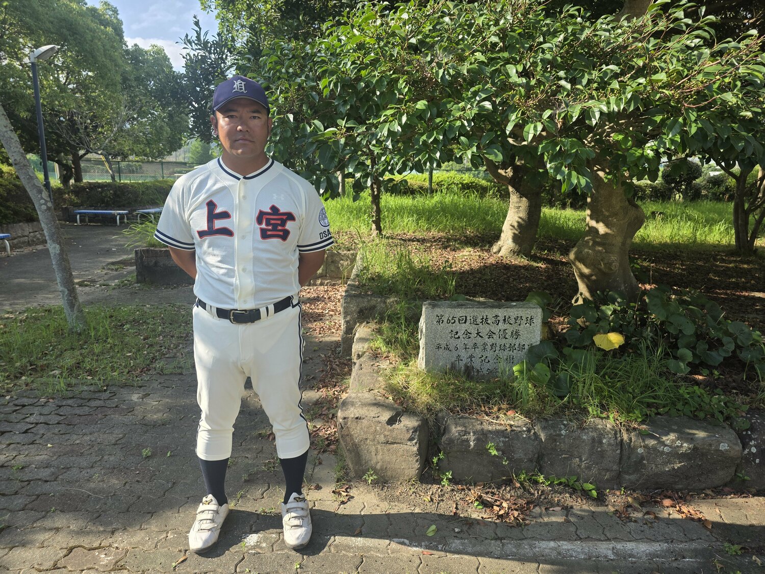 1993年センバツ優勝の記念樹と石碑の前に立つ村田監督 ©Katsuharu Uchida