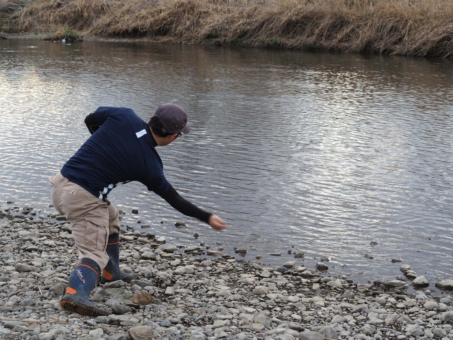 橋本さんは野球のアンダースローのようなフォームで川に投げ込む