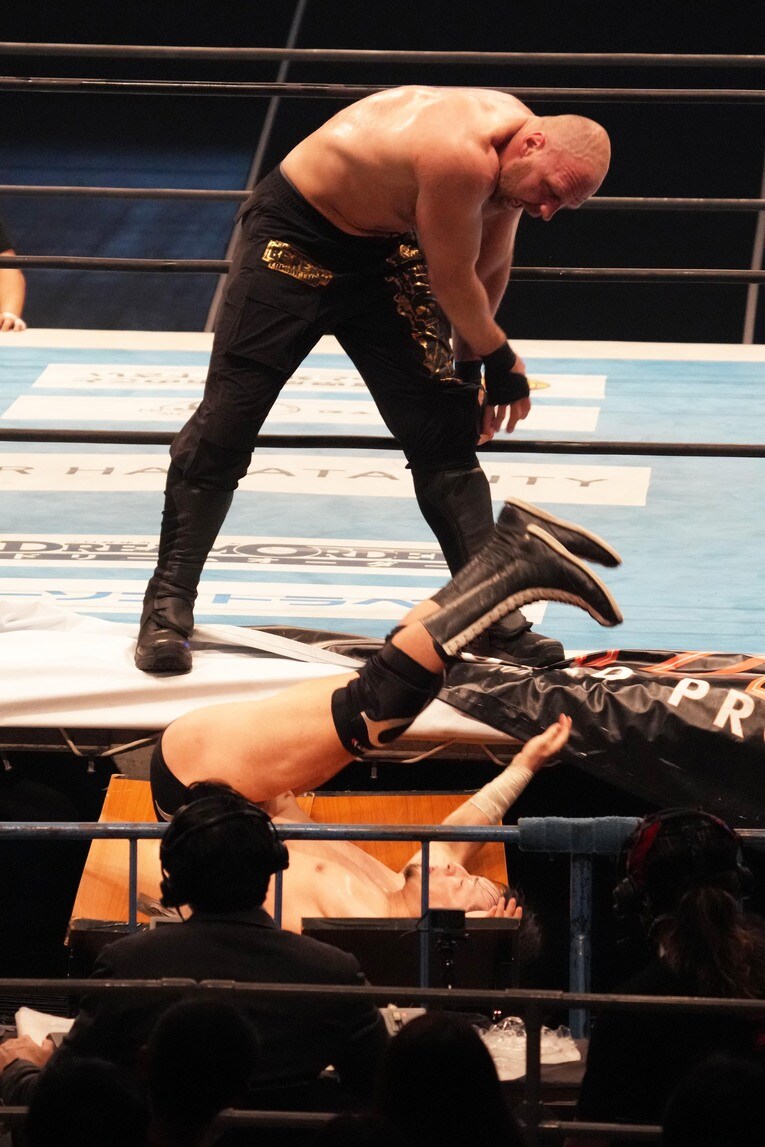 場外のテーブルに成田蓮を叩きつけるジョン・モクスリー　©Essei Hara