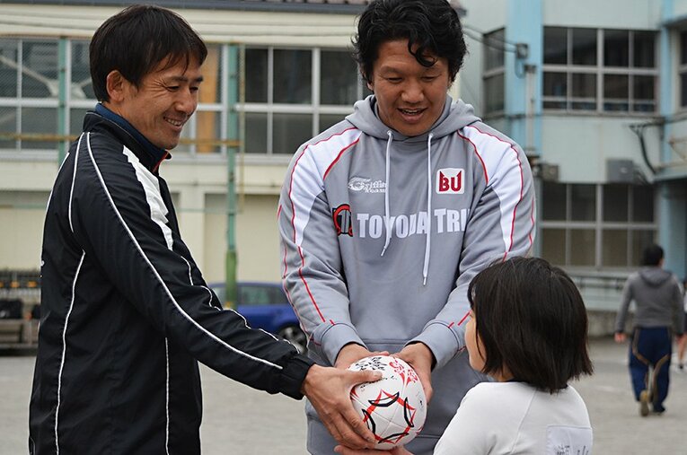子供達にラグビーボールを配る小野澤宏時（左）と菊谷崇。ラグビーへの熱を絶やさぬよう、「たくさん汚してね」と語りかける姿が印象的だった。 ／ photograph by Masataka Tara