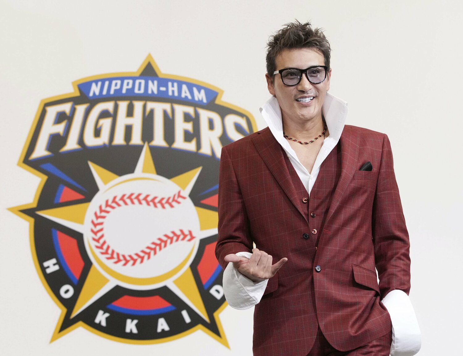 ファイターズのロゴを背に、赤のスーツに大きな襟を立てた白シャツは胸元を開けていて、首元には赤のネックレスが。カメラに向ってアロハポーズも決めた　©KYODO