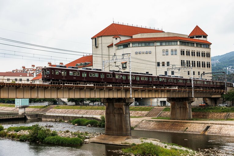 武庫川の橋を渡る阪急電車。その奥に宝塚歌劇団の本拠地・宝塚大劇場が見える