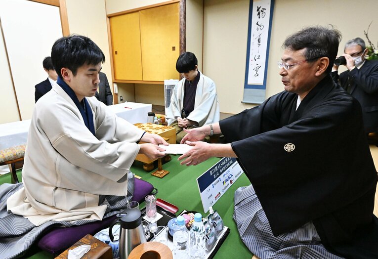 立会の塚田泰明九段に封じ手を渡す挑戦者の菅井八段（代表撮影）　©JIJI PRESS