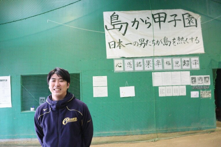隠岐高・渡部謙監督。室内練習場には「島から甲子園」の文字。2003年以来の出場を目指す　©Yuki Kashimoto