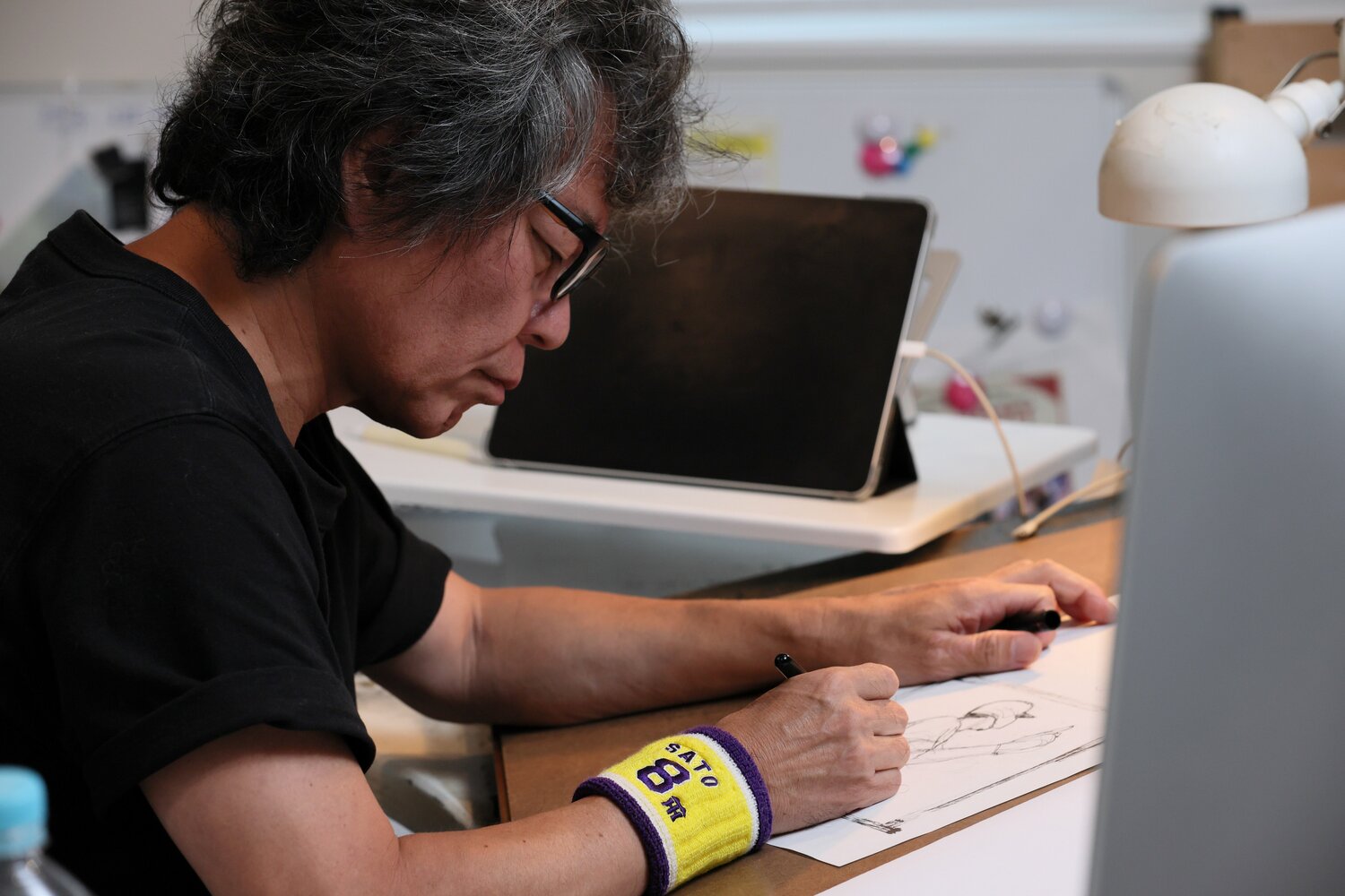 「SATO 8」と刺繍されたリストバンドをつけ、サラサラと佐藤輝明のホームランシーンを描く髙橋氏　©Shigeki Yamamoto