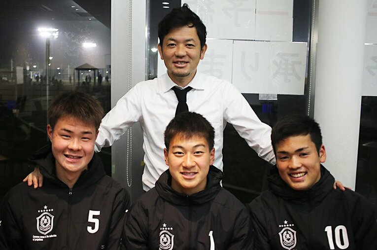 興國高校・内野智章監督（上）と写真に収まる平井、田川、樺山（左から）。2年生トリオは早々にマリノス内定を勝ち取った。 ／ photograph by Takahito Ando