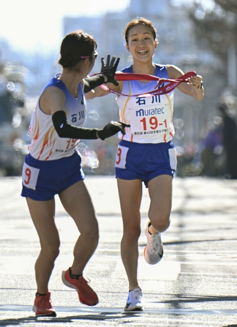 1区を区間賞の快走で駆け抜け、2区の猿見田裕香（左）に笑顔で襷を渡す五島　©︎KYODO
