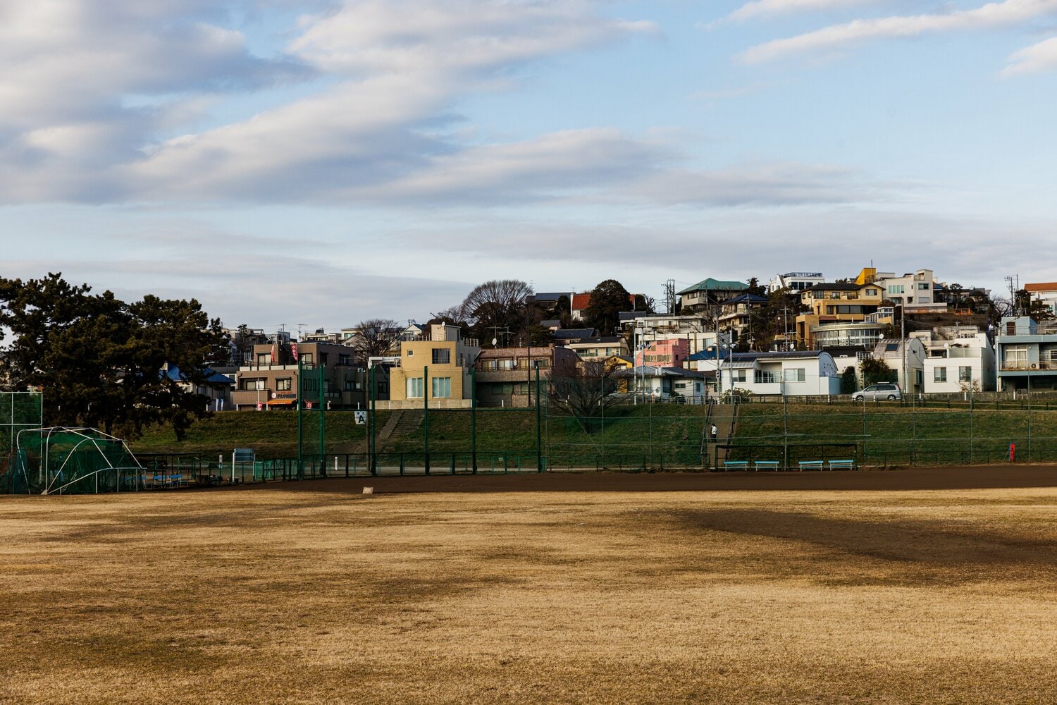 外野側から野球場を見る。土手の向こう（左）に、巨人の選手たちも通ったという商店（小池商店）が見える