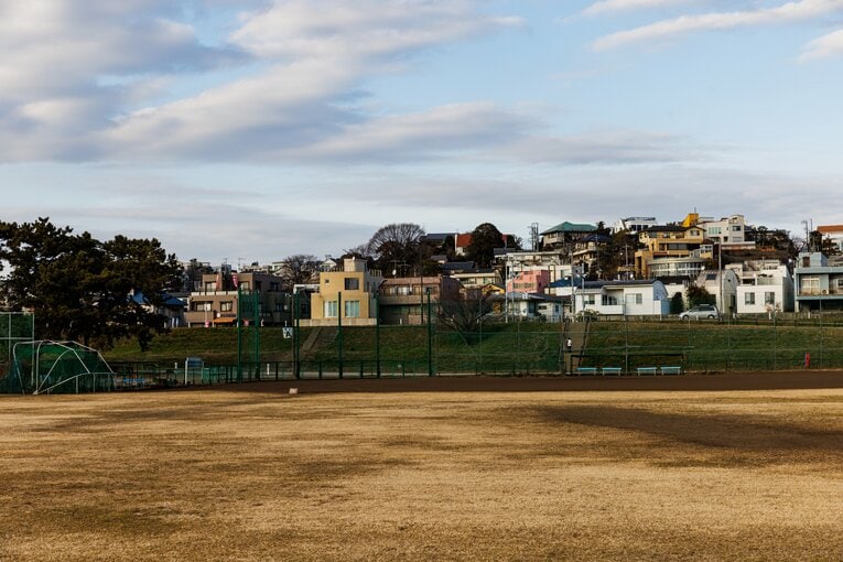 外野側から野球場を見る。土手の向こう（左）に、巨人の選手たちも通ったという商店（小池商店）が見える