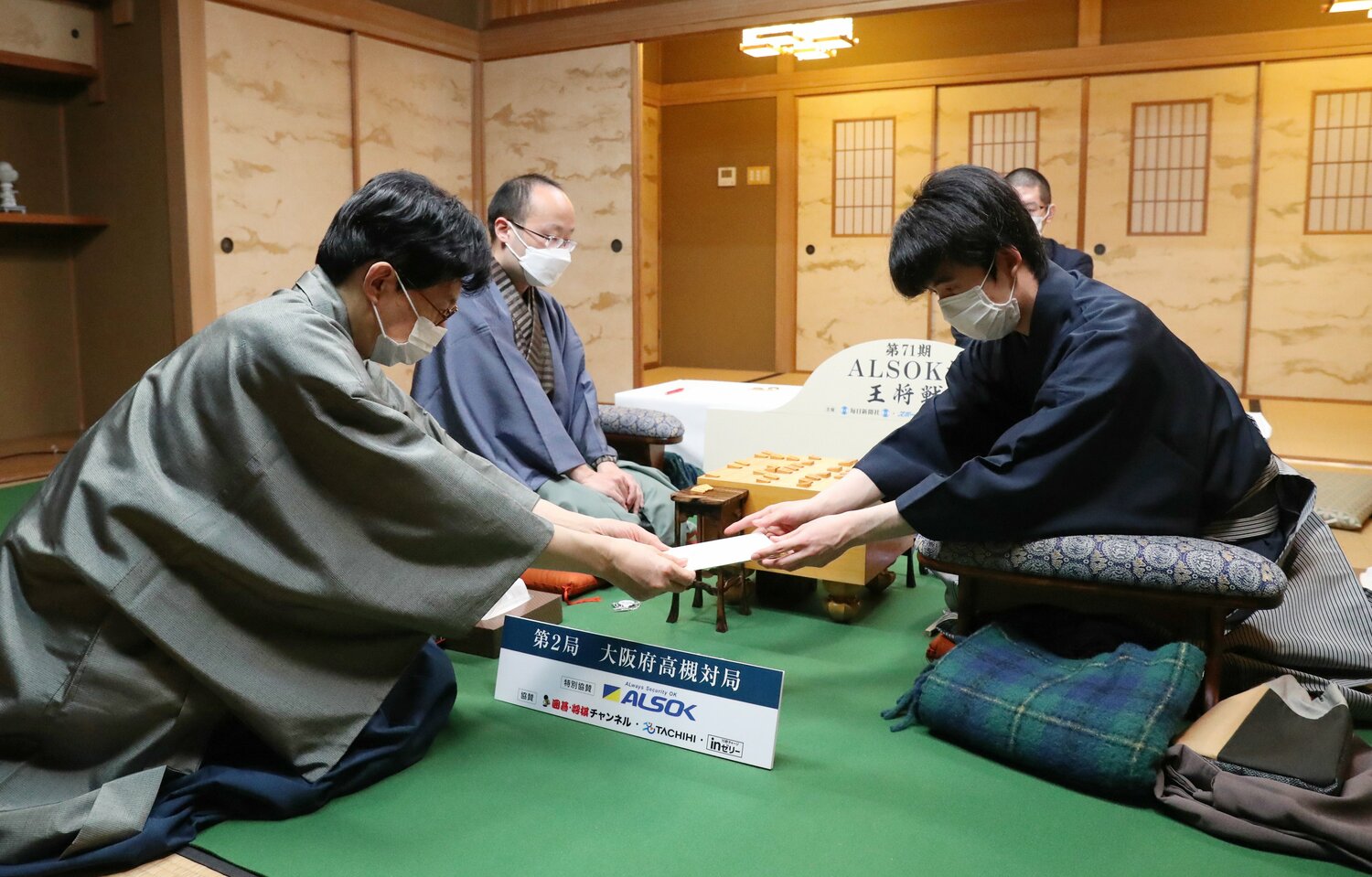 第71期王将戦7番勝負第2局1日目。立会人の谷川浩司九段（左）に封じ手を渡す藤井聡太四冠。左奥は渡辺明王将（段位は当時） ©JIJI PRESS