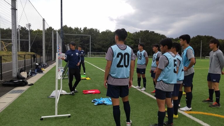ホワイトボードを使って選手役の大学生たちに戦術を伝える中村憲剛さん　©JFA