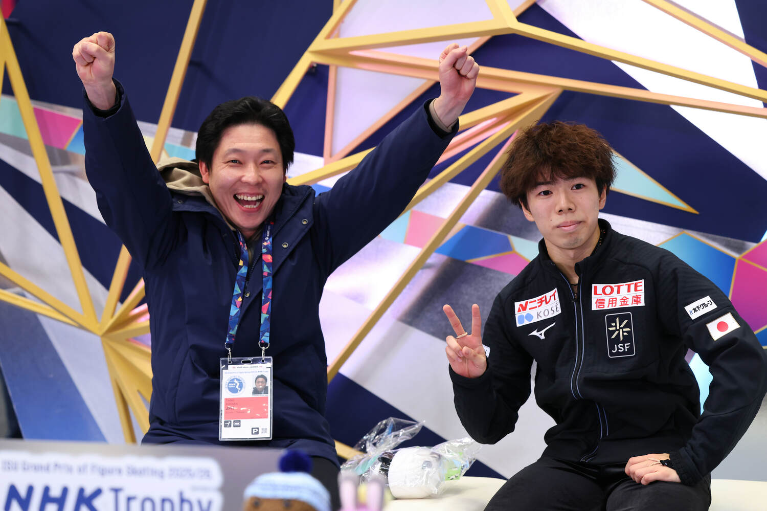 NHK杯フリー演技の得点が出て、ガッツポーズの日下匡力コーチ（左）と小さくピースの佐藤駿　©️AFLO