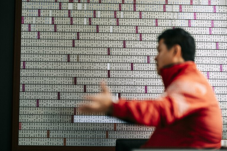 歴代の選手たちの名前が飾られたボードの横でインタビューに応じた大田尾監督　©︎Kiichi Matsumoto