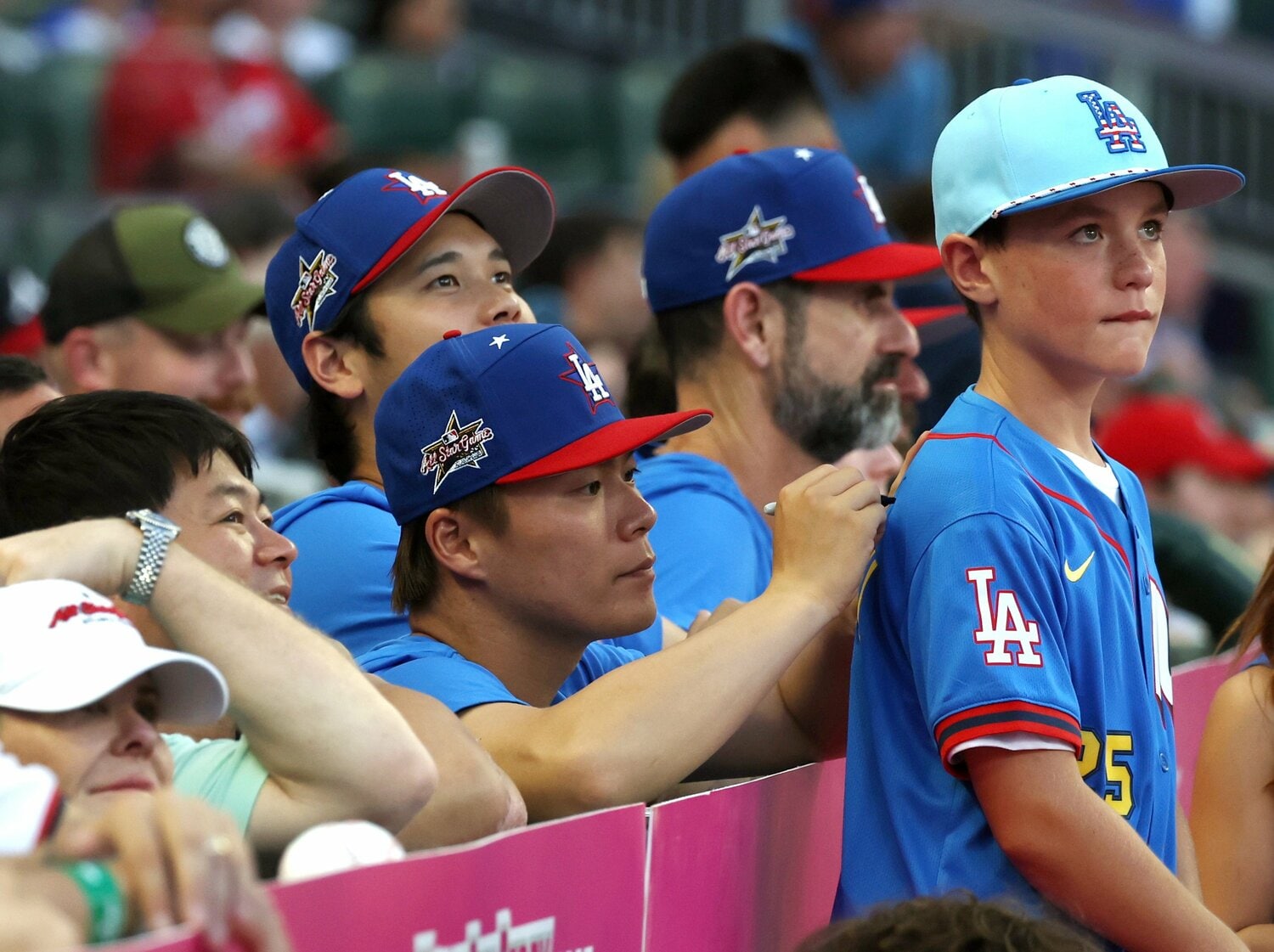 オールスター戦前日の本塁打競争をベンチから観戦し、子どものユニホームにサインをする山本由伸　©JIJI PRESS