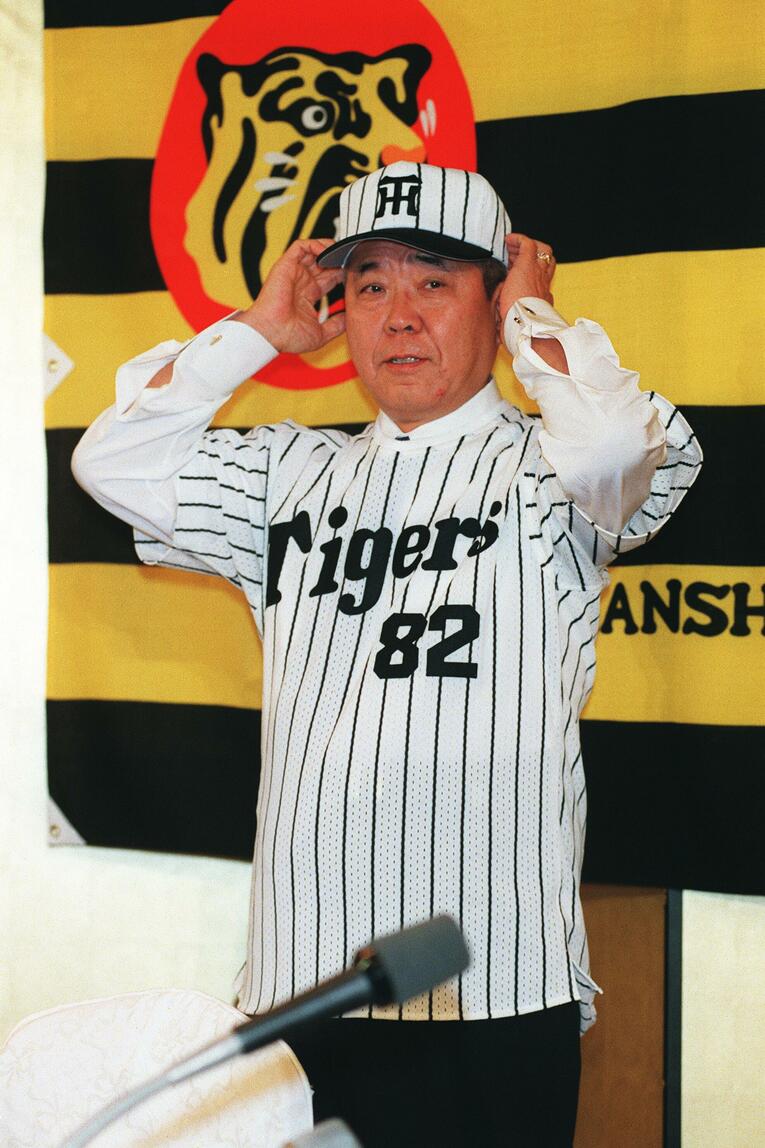 阪神タイガース監督就任会見で真新しい縦縞のユニフォームにそでを通す野村監督　©︎JIJI PRESS