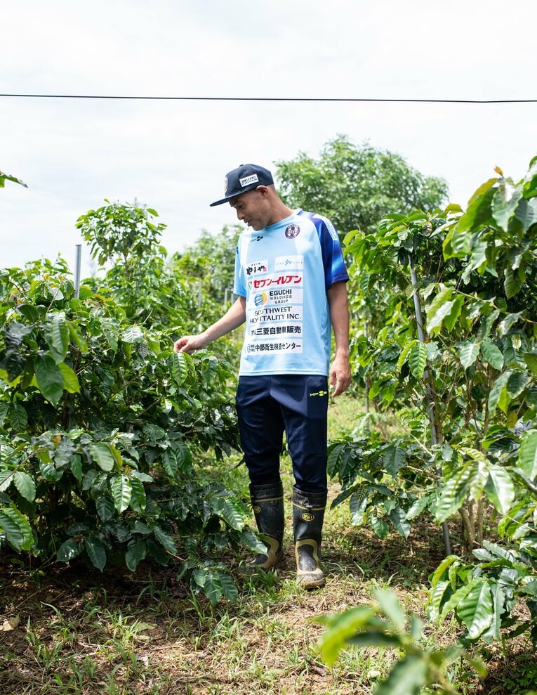 マイ長靴を履き、コーヒー畑に立つ高原直泰（43歳）。沖縄SV（九州リーグ）のCEOも務める　©Nanae Suzuki