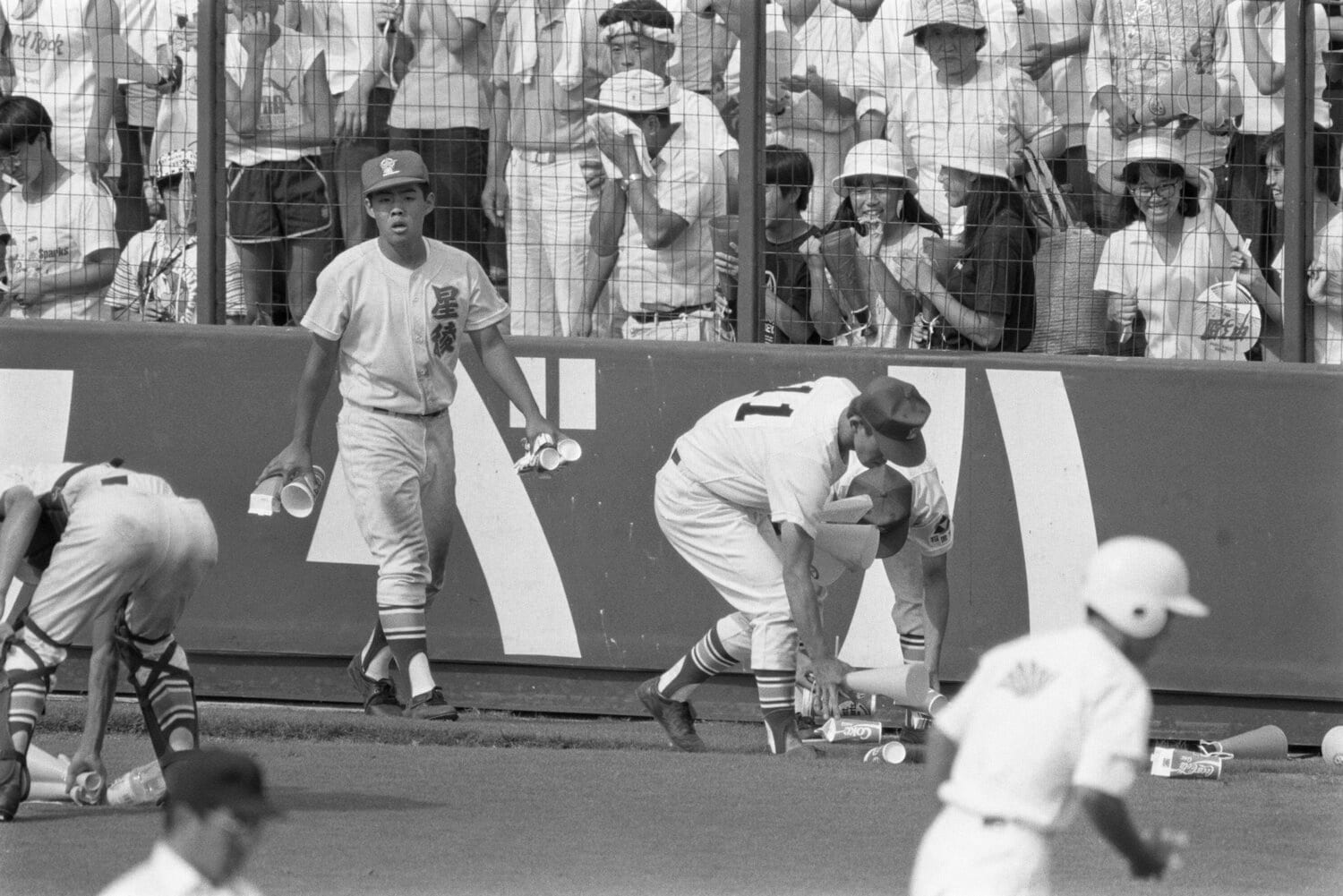 グラウンドに投げ込まれたコップやメガホンを拾う星稜の選手たち　©JIJI PRESS