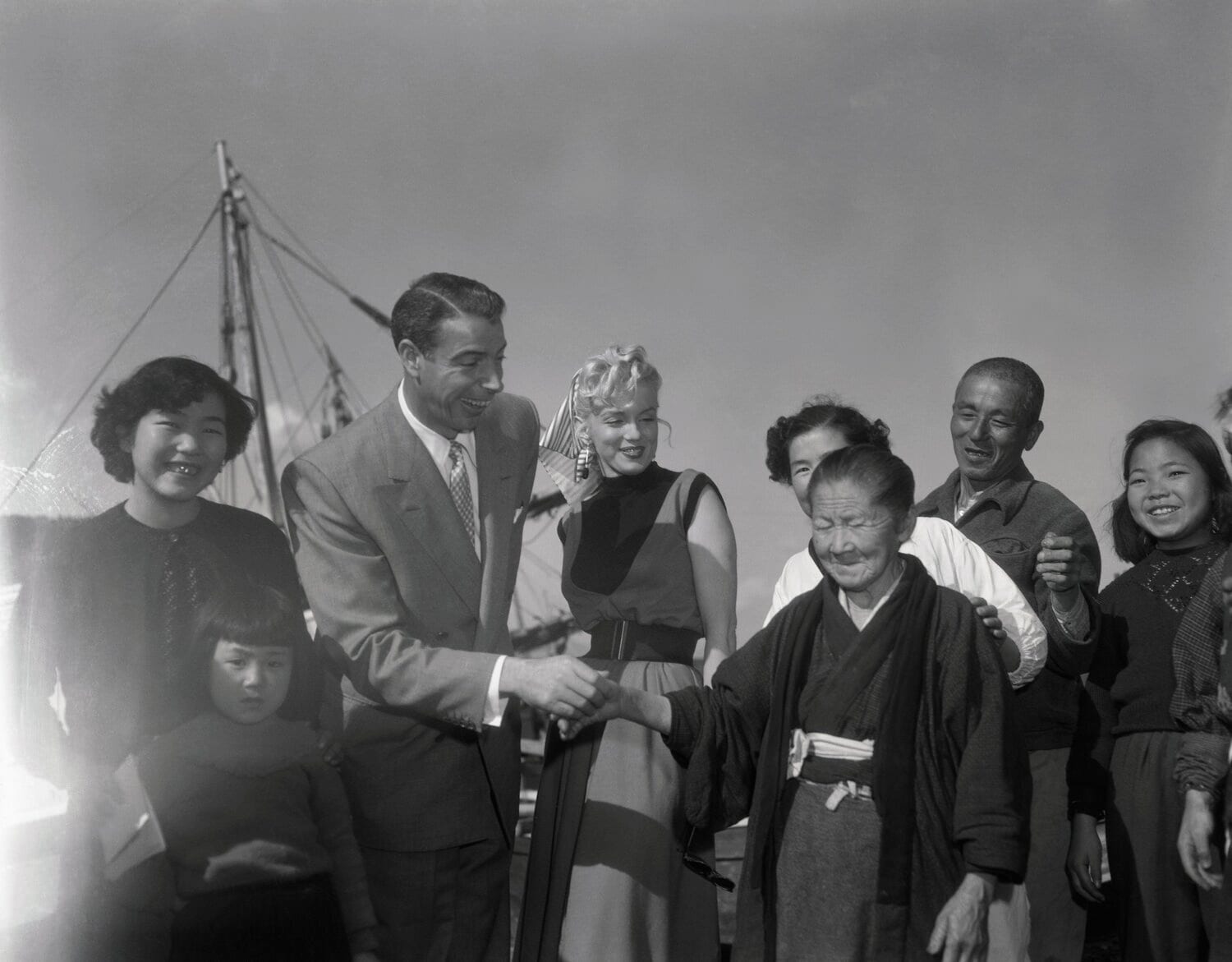 1954年、マリリン・モンローと新婚旅行で日本を訪れたジョー・ディマジオ【1枚目／全2枚】。記念写真で握手をする　©Getty Images