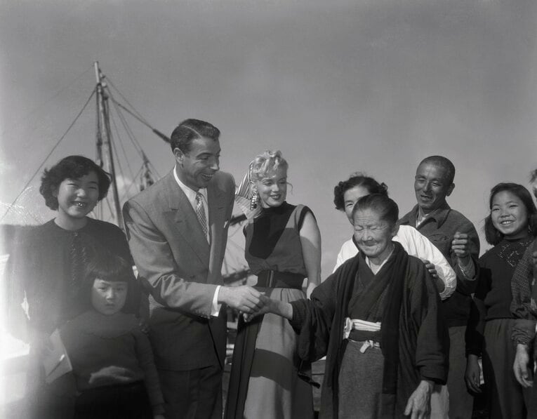 1954年、マリリン・モンローと新婚旅行で日本を訪れたジョー・ディマジオ【1枚目／全2枚】。記念写真で握手をする　©Getty Images