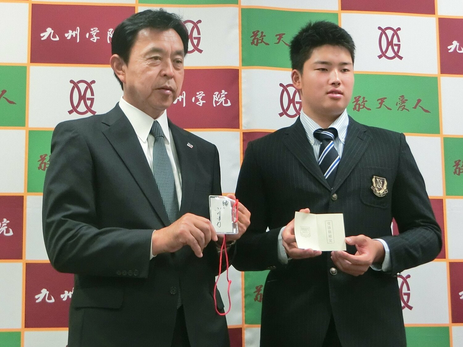 1位指名した九州学院高・村上宗隆に、抽選の当たりくじと、ドラフト会議時に首から提げていたホルダーに「縁」と書いて手渡すヤクルトの小川淳司監督 ©JIJI PRESS
