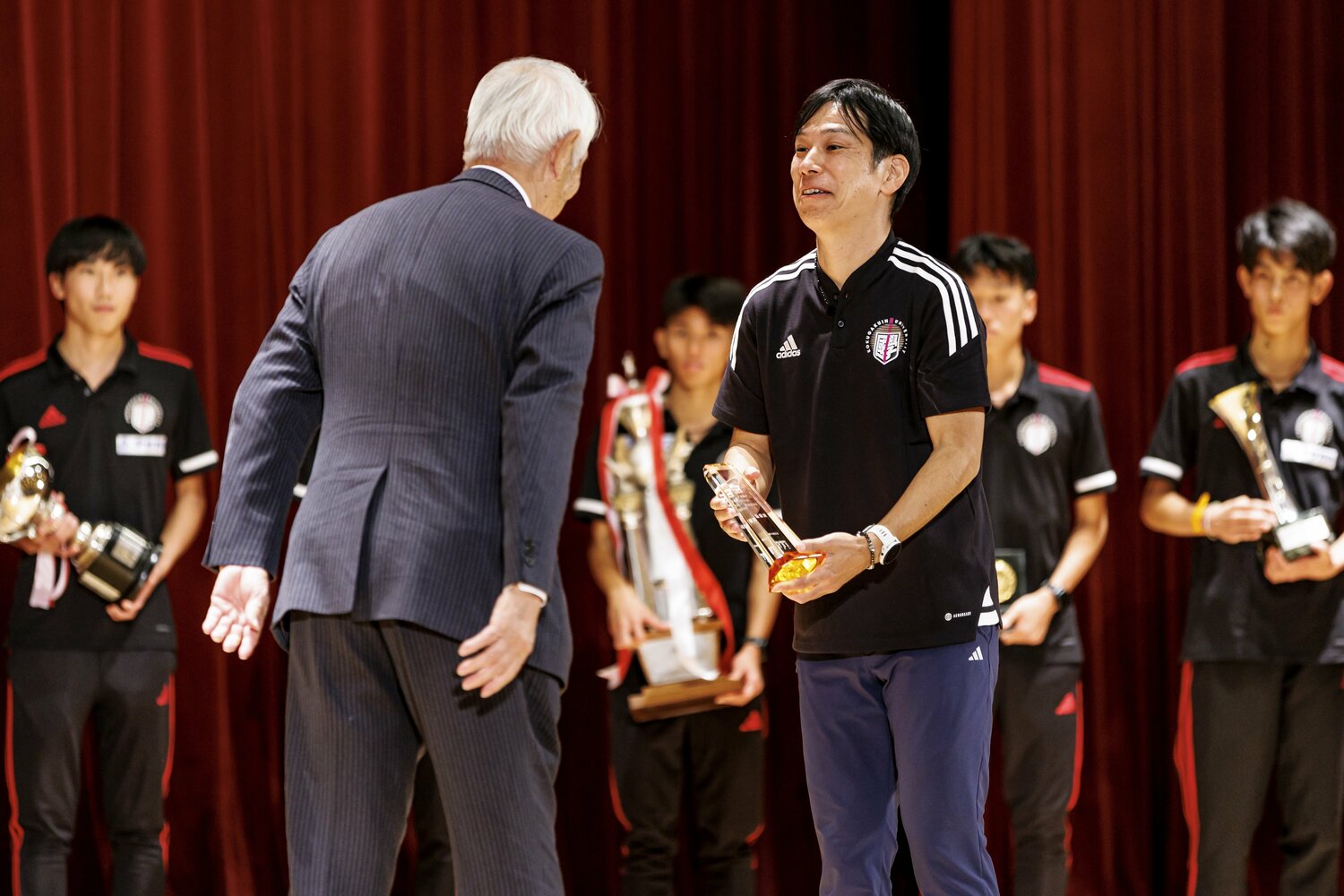 笑顔でトロフィーを受け取る前田監督　©Kiichi Matsumoto