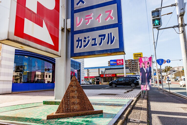 南小倉駅から国道3号を15分ほど歩くと…紳士服のはるやまがあった。その大きな看板の足元にあるのは…「小倉到津球場跡」（写真中央、読みづらいがそう書いてある）の小さな石碑だった　©Masashi Soiri