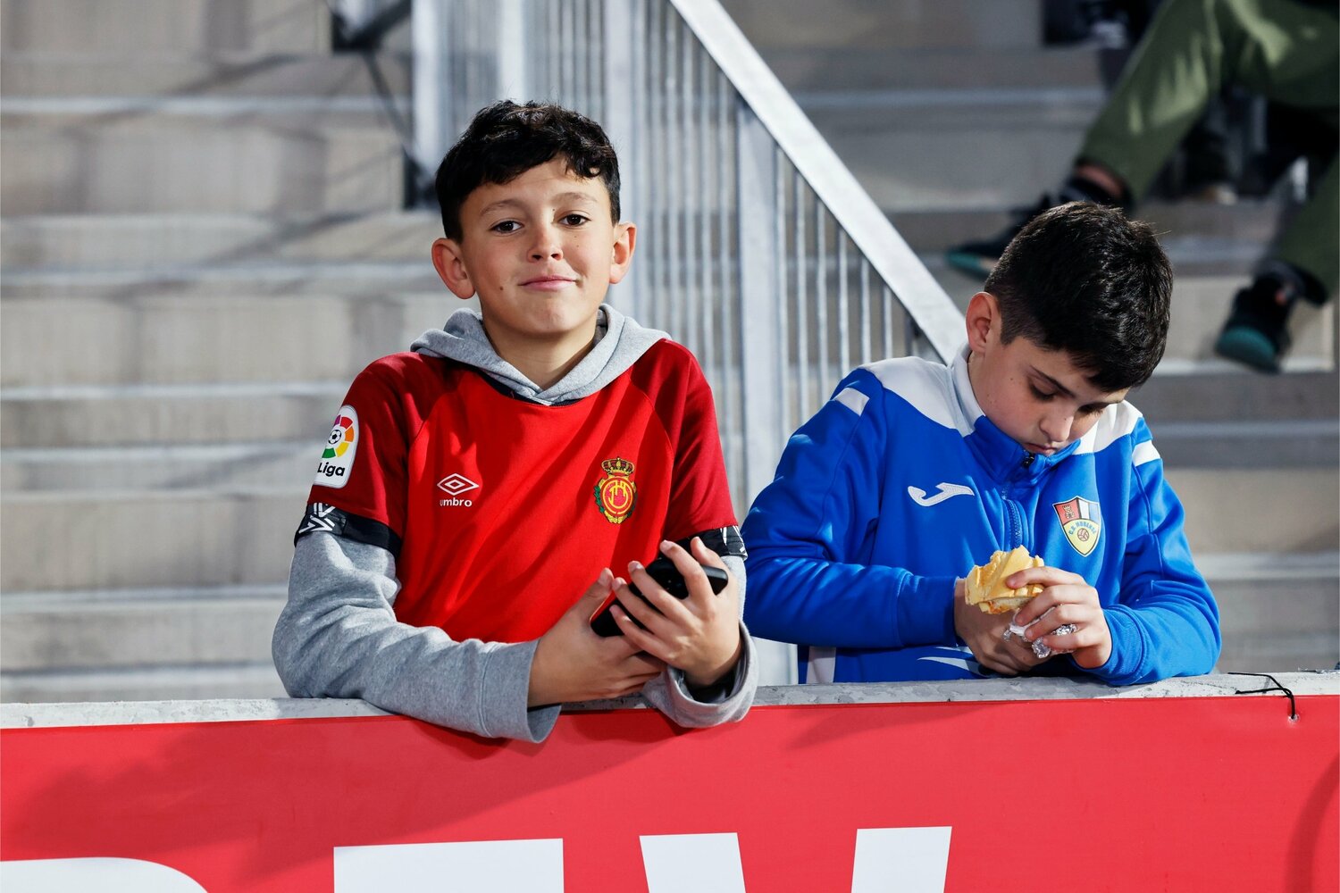 最前列で〈KUBO！〉と大きな歓声を上げていたマジョルカユニホームの少年と、パンに夢中の少年サポ