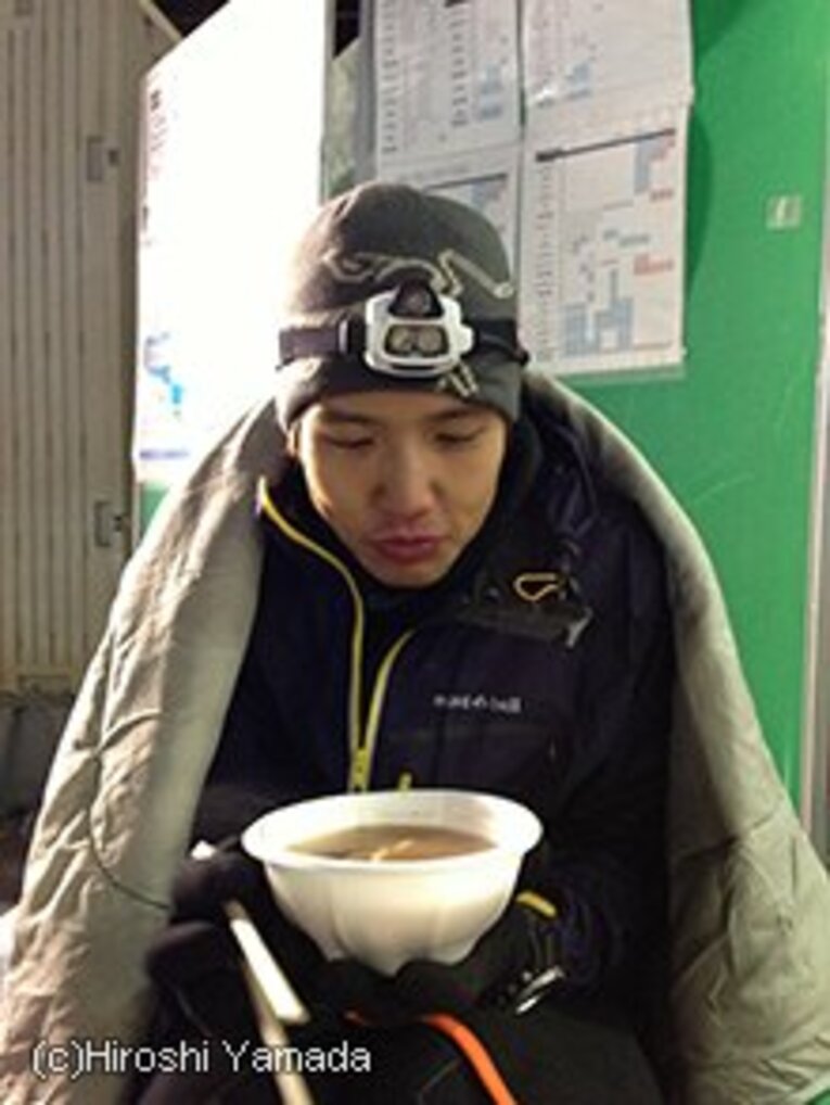 ストーブの前で毛布をかけられ、豚汁を飲む武田。