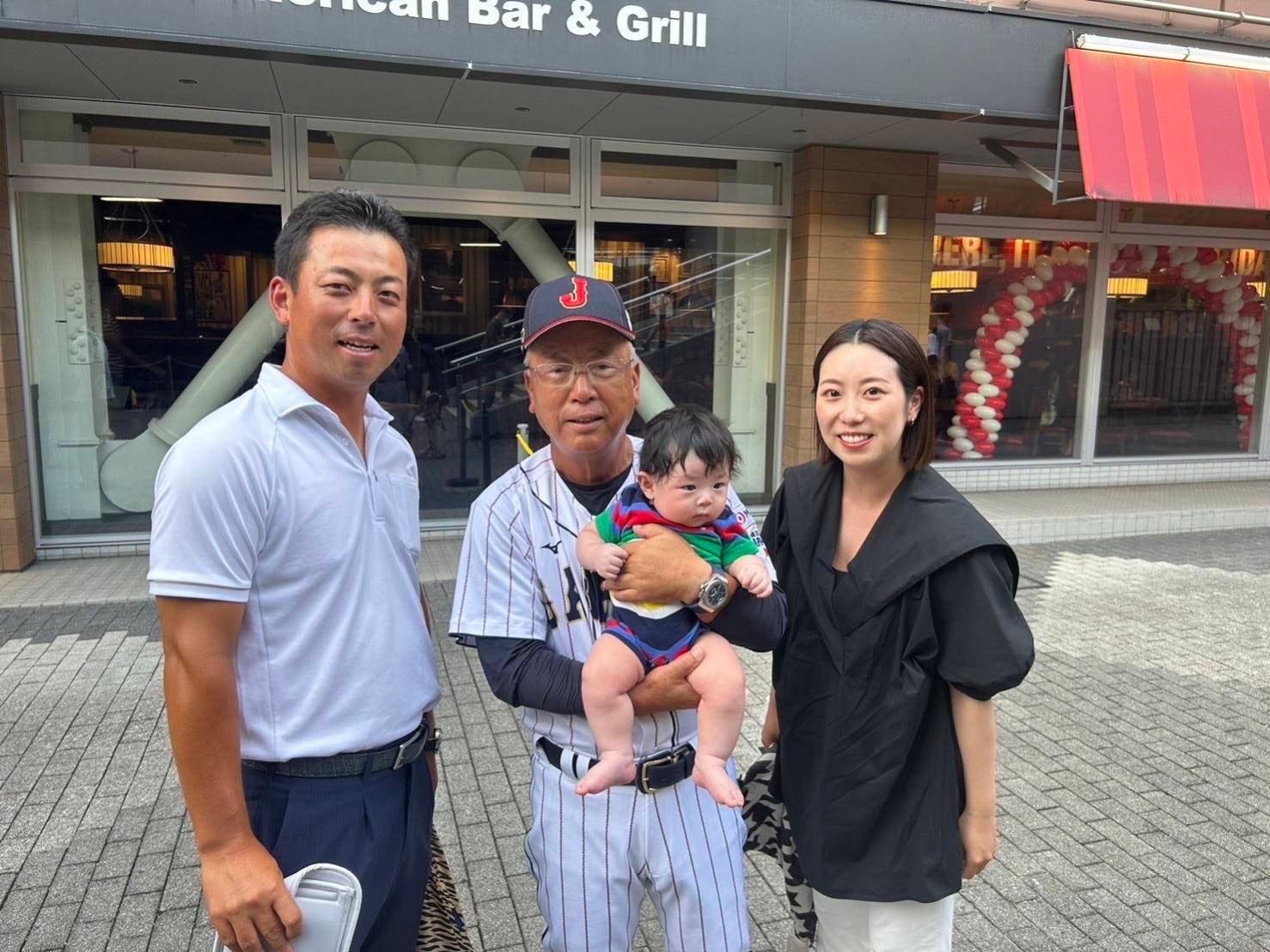 孫の遼正（りょうま）くんを抱っこし笑顔の馬淵史郎監督（中央）。侍ジャパンU-18 代表の試合は、烈（左）も妻の美香さんと遼正くんと一緒に応援した　©本人提供