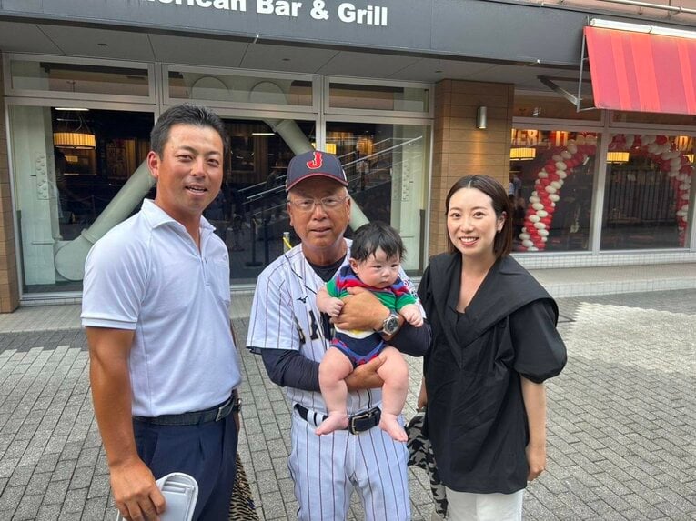 孫の遼正（りょうま）くんを抱っこし笑顔の馬淵史郎監督（中央）。侍ジャパンU-18 代表の試合は、烈（左）も妻の美香さんと遼正くんと一緒に応援した　©本人提供