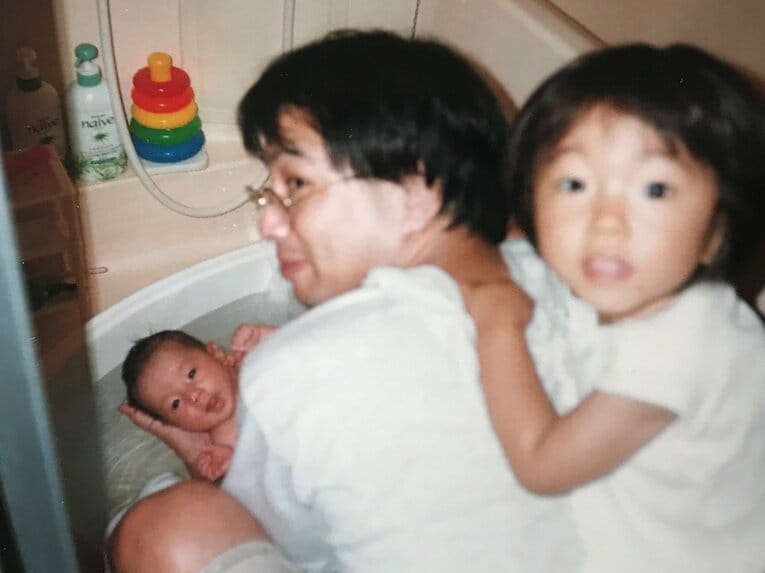 長女を背中におぶって次女をお風呂に入れる日高邦博　※本人提供