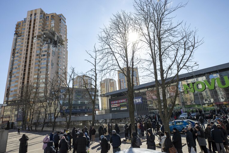 ロシア軍の砲撃で破壊された高層住宅と、物資を得るためにスーパーの列に並ぶキエフ市民　©Getty Images