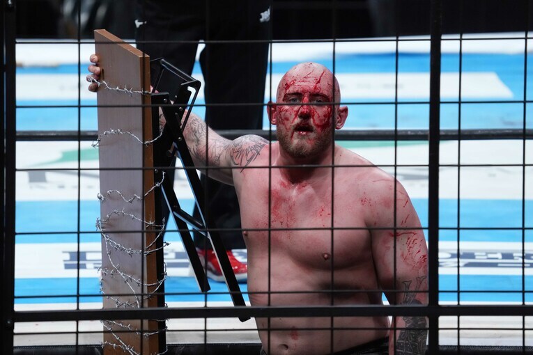 檻の中で有刺鉄線を巻いたテーブルを手にするゲイブ・キッド　©Essei Hara