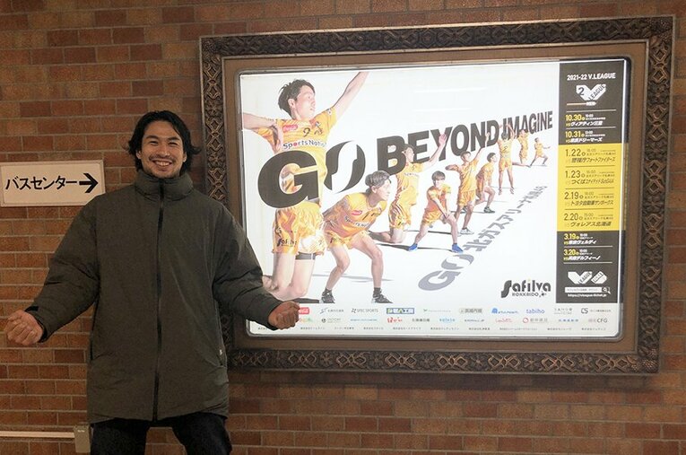 札幌市内の街中にポスターを見つけ、笑顔で写真に収まる柳川大知。仕事をしながらプレーする仲間たちの思いをデザインに込めた ／ photograph by Safilva Hokkaido