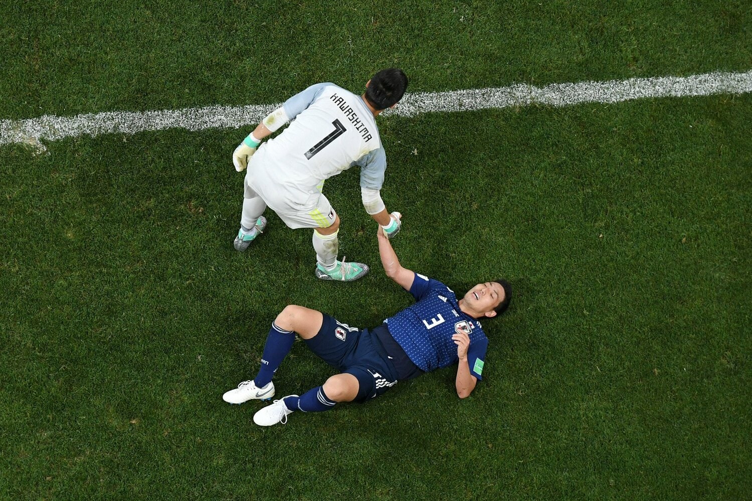 グラウンドに寝転ぶ昌子に手を差し伸べるGK川島　©︎Getty Images