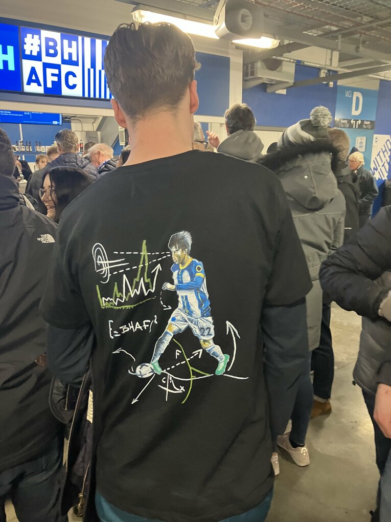 ブライトンファンのなかには三笘のオリジナルTシャツを着る人も（1／2枚）。ちなみにTシャツはイギリスのオンライン・サッカーグッズショップで販売されているが現在品切れ中だという