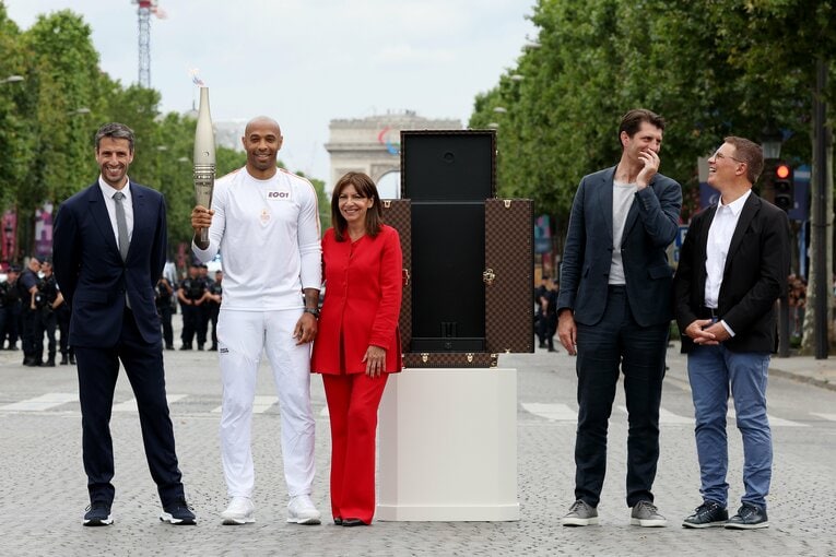 聖火ランナーのアンリ監督（左から2番目）らとバッチリ写真に収まるイダルゴ市長（赤スーツ）。隣に鎮座するのがルイ・ヴィトン謹製トーチ・トランクである　©Getty Images